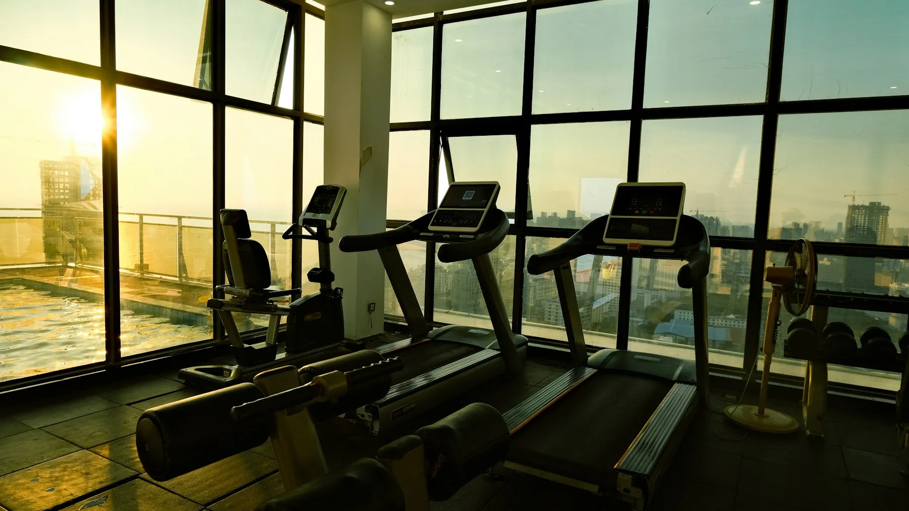 Treadmills and an exercise cycle by tall, sunlit windows